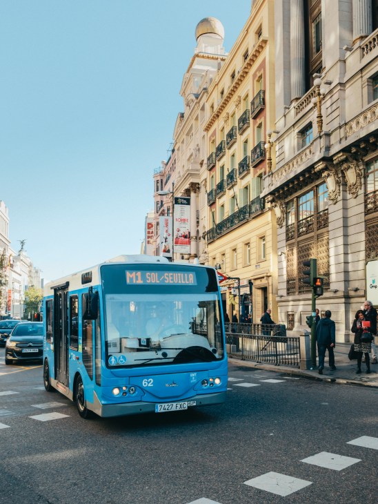 Blue electric microbus numbered 62 on a Madrid street lined with historic buildings.
