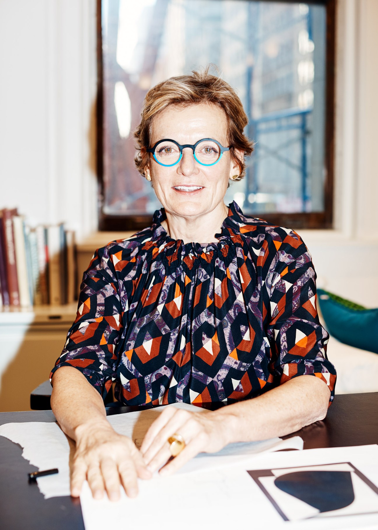 Alexandra Champalimaud at her New York design studio desk wearing blue-framed glasses and patterned shirt