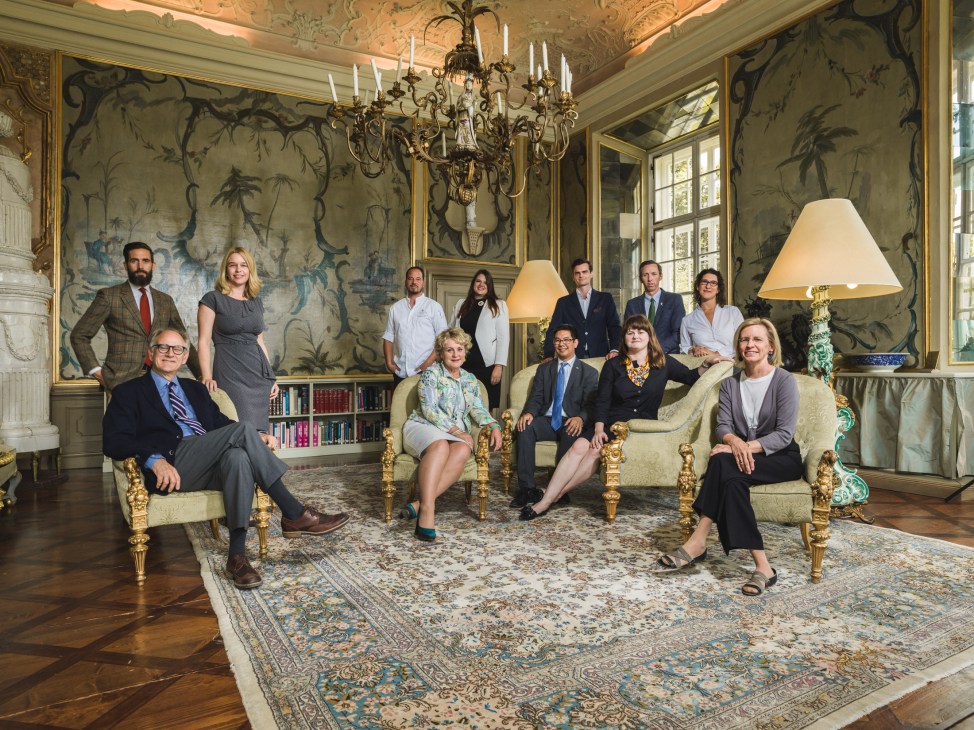 Team of Salzburg Global Seminar staff posed in an ornate 18th-century palace room with chinoiserie wallpaper and crystal chandelier.