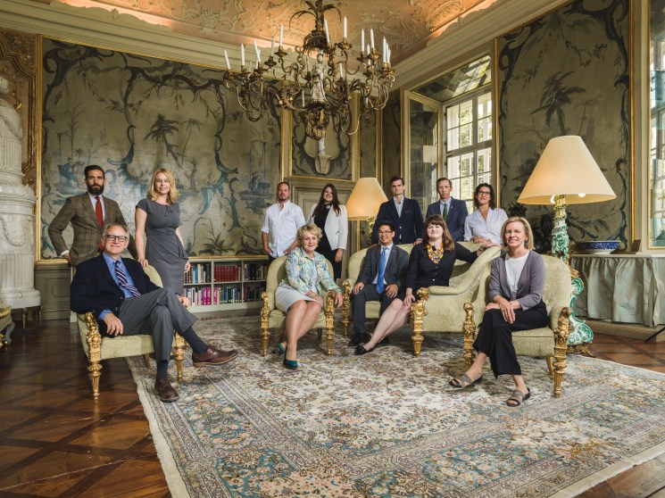 Team of Salzburg Global Seminar staff posed in an ornate 18th-century palace room with chinoiserie wallpaper and crystal chandelier.