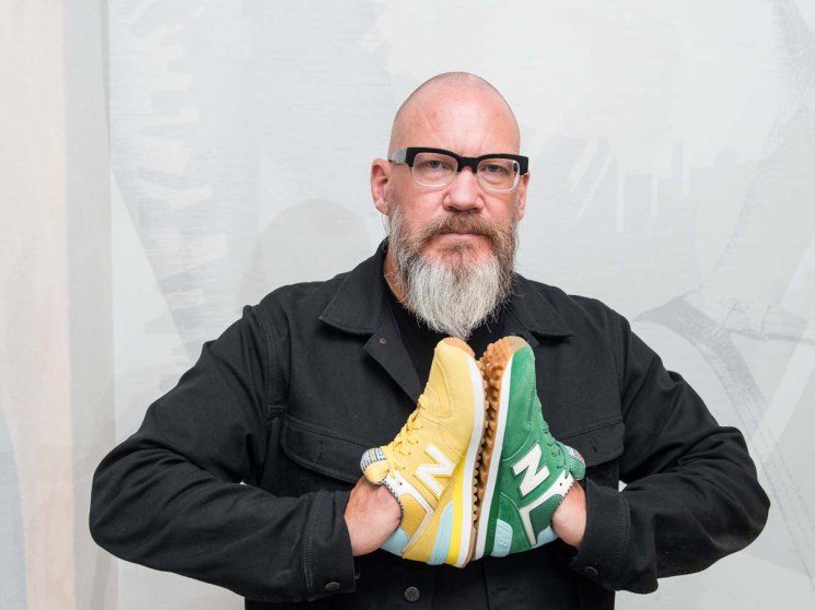 Bob Neville, New Balance's global retail creative director, holds yellow and green New Balance sneakers while wearing glasses and a black jacket.