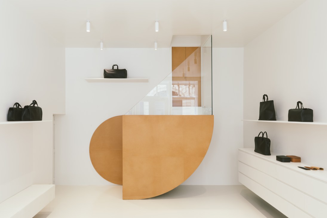 Isaac Reina's Paris shop interior with minimalist white walls, angular leather tabletops, and displayed black leather bags.