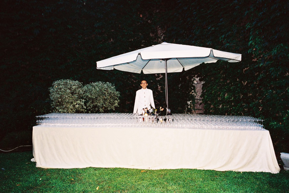 French ambassador Christian Masset stands under a white umbrella at a table during the Fête Nationale celebration at Palazzo Farnese.