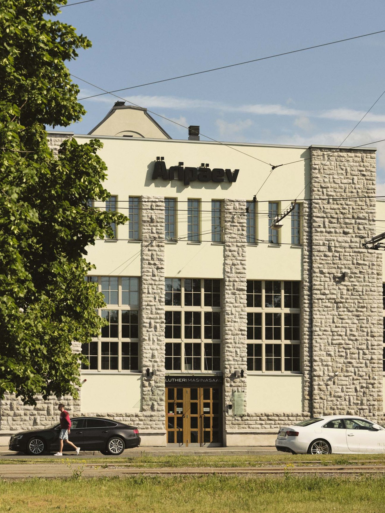 Aripaev newspaper building in Tallinn with limestone and concrete facade, large windows, and ivy-covered trees.