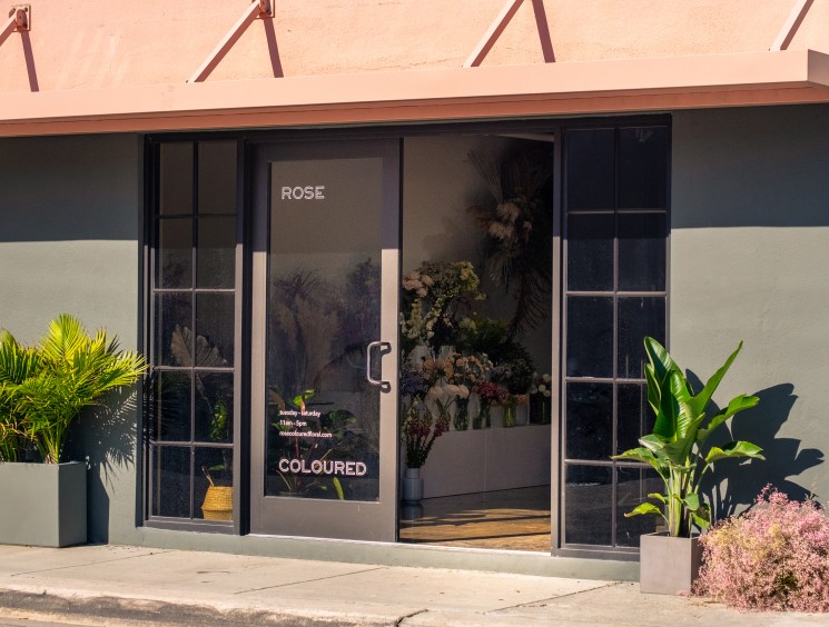 Storefront of Rose Coloured Floral shop in Little River with flowers displayed in window and potted plants outside.