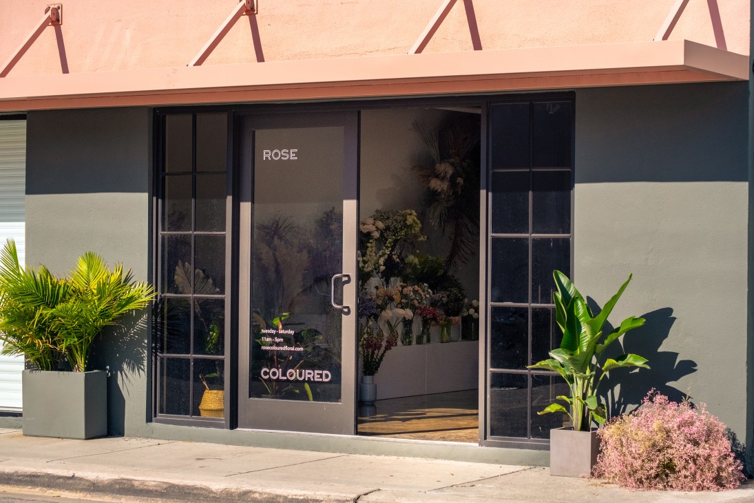 Storefront of Rose Coloured Floral shop in Little River with flowers displayed in window and potted plants outside.