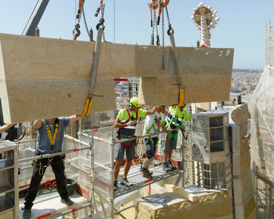 Construction workers guide a granite slab suspended by crane onto the Sagrada Família roof in Barcelona.