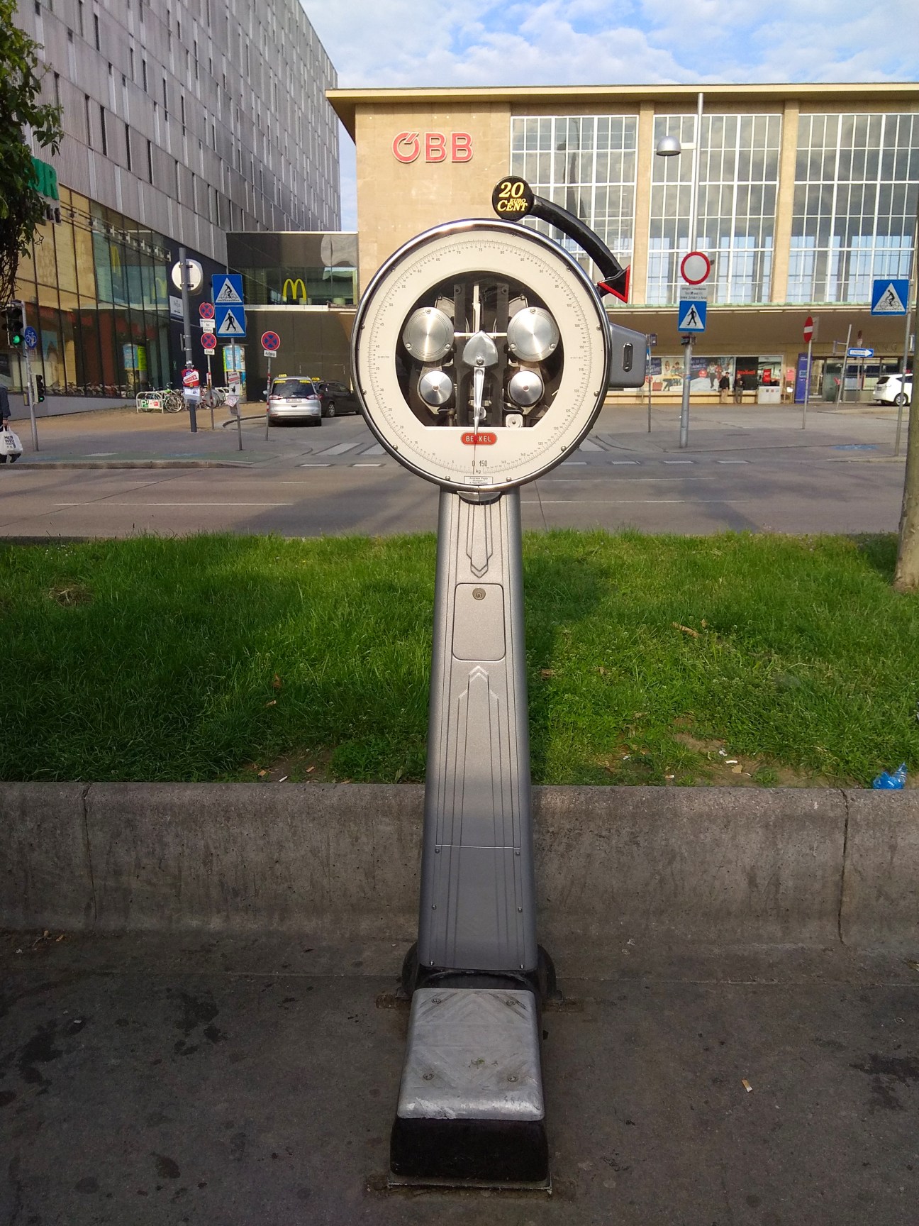 A vintage weighing scale on a sidewalk, in front of a building in the background.