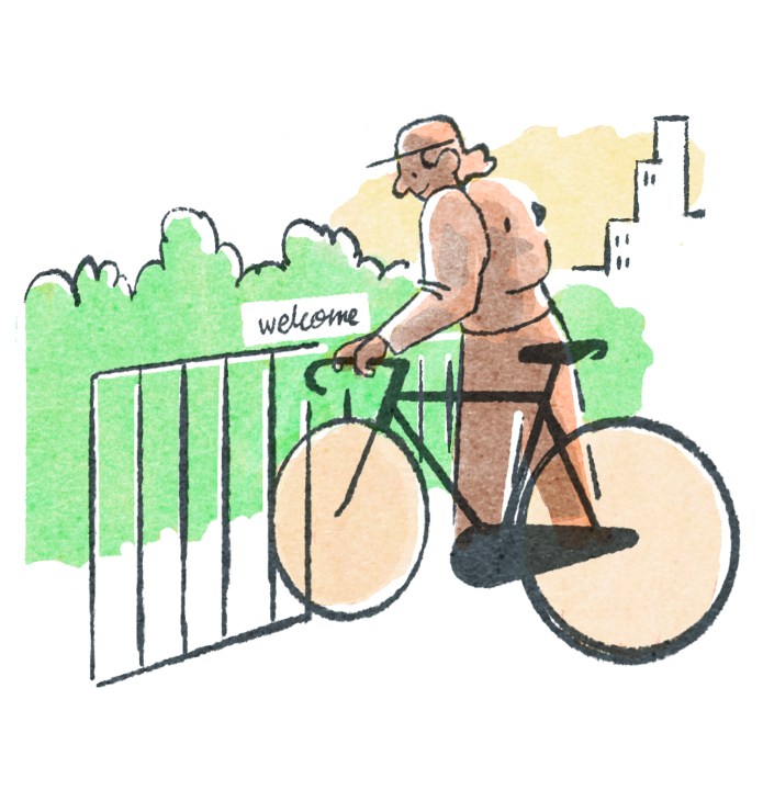 Person on bicycle arriving at a welcoming gate with hedges and buildings visible in the background