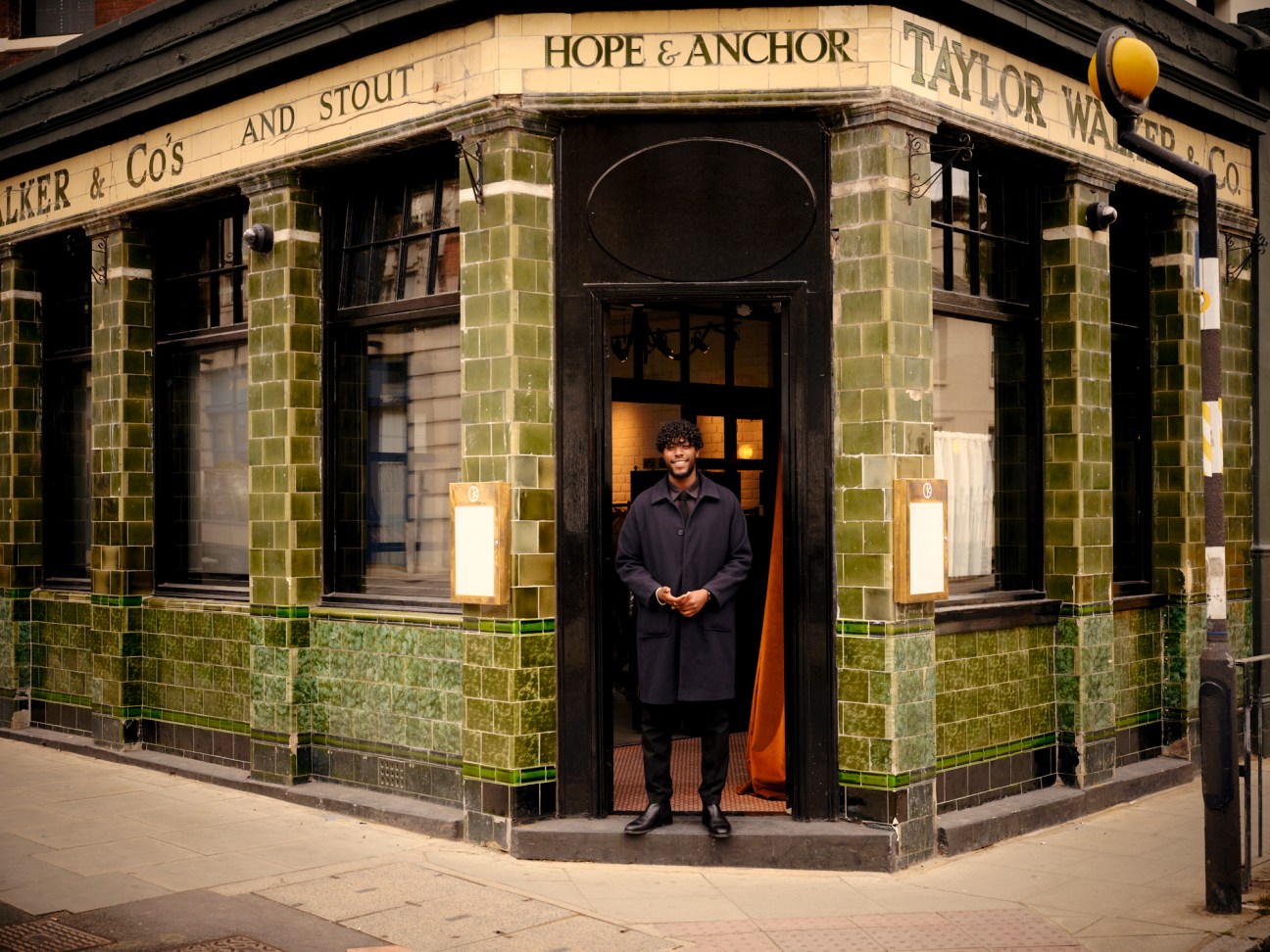 Person standing in the doorway of a historic pub entrance with traditional green Victorian tilework