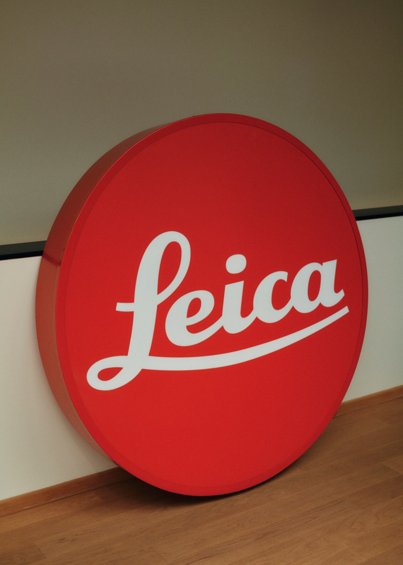 Red circular Leica logo sign with white script lettering displayed indoors