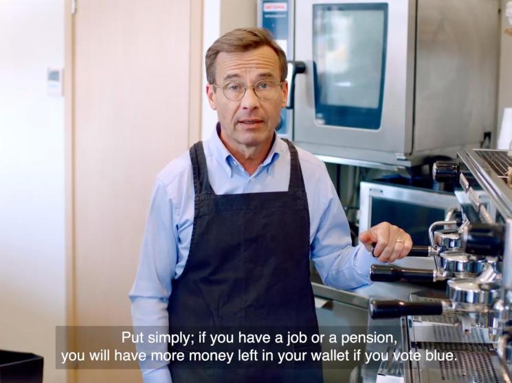 Man in apron and glasses standing in kitchen speaking to camera with subtitle about voting blue