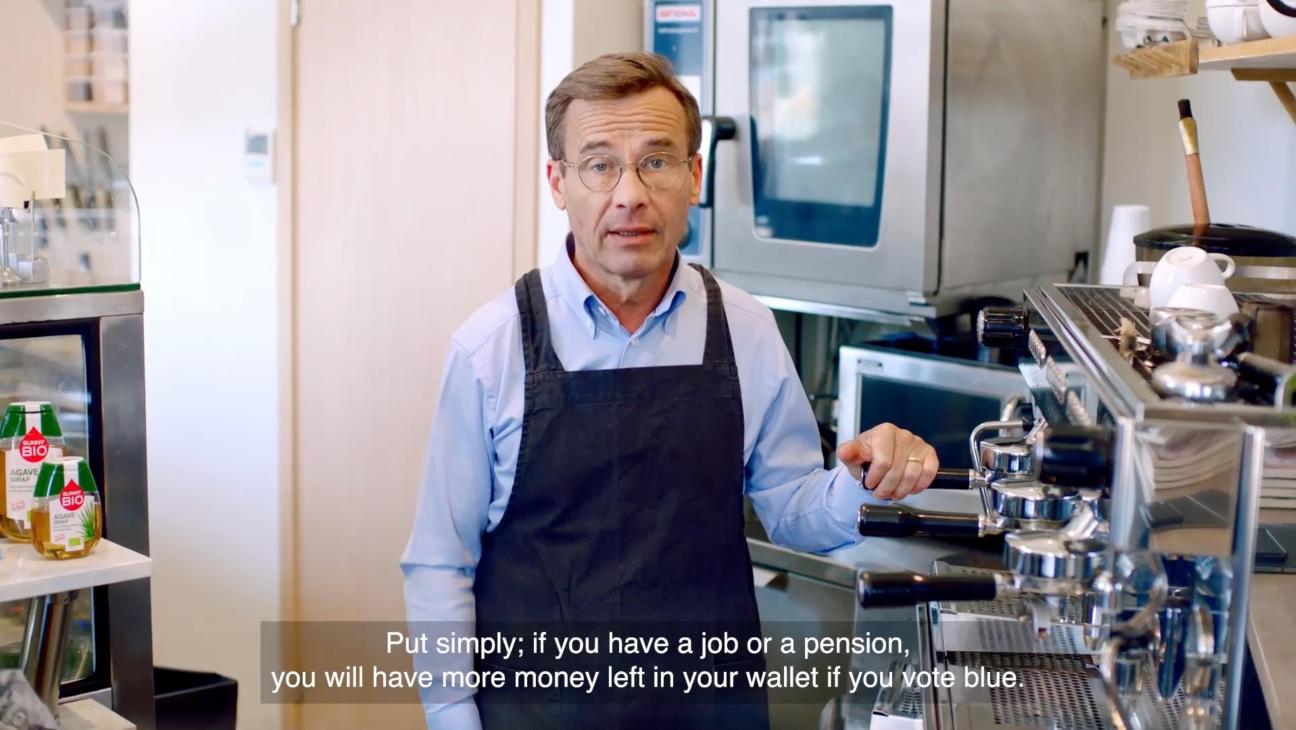 Man in apron and glasses standing in kitchen speaking to camera with subtitle about voting blue