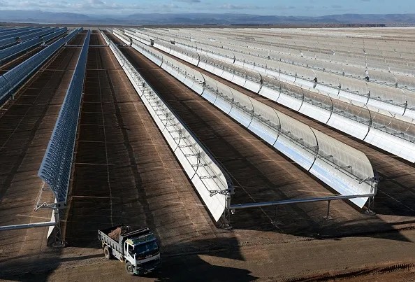 Aerial view of concentrated solar power plant with parallel rows of solar collectors in desert landscape.