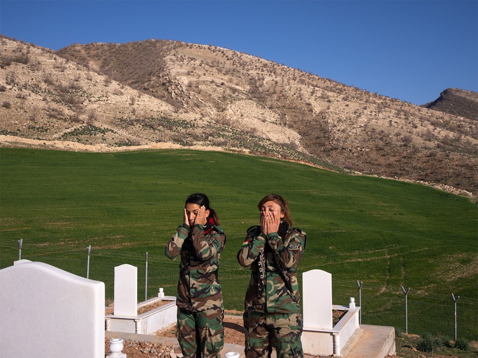 Two PAK fighters kneeling and praying at gravestones in a cemetery