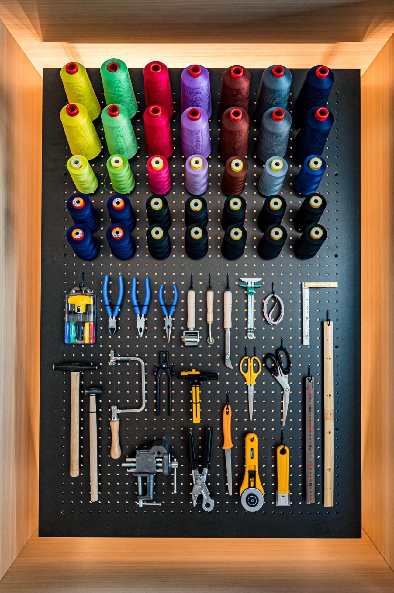 Organized pegboard wall displaying colorful spools of thread, scissors, pliers, and various sewing and craft tools.