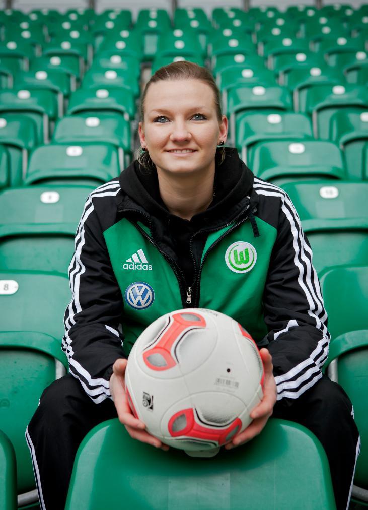Alex Popp, German footballer for VfL Wolfsburg, holds a soccer ball while seated in stadium stands.
