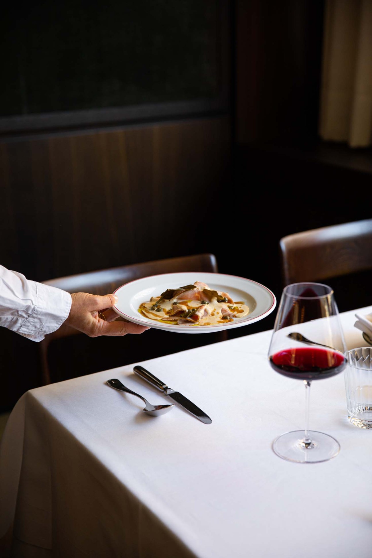 Dish getting placed at a table with red wine 