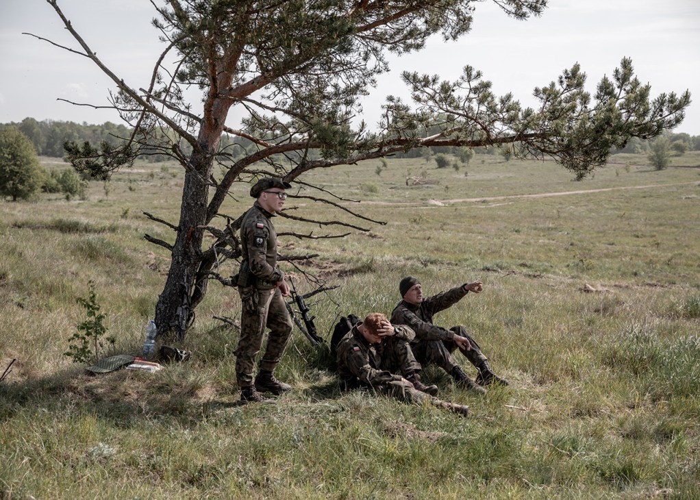 Three Polish soldiers rest underneath a tree between exercises
