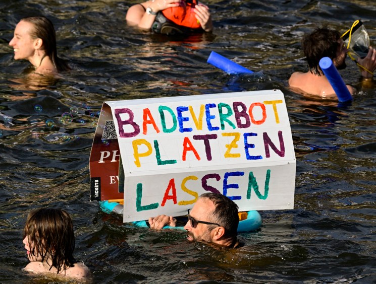 A participant swims with a placard with the lettering 'Break the bathing ban' while taking a dip in the Spree river during a second swimming demonstration for the abolition of the general swimming ban in the inner-city Spree river in central Berlin on August 12, 2025. They demonstrate for the possibility to swim in the inner-city Spree river again; it was banned around 100 years ago. (Photo by John MACDOUGALL / AFP) (Photo by JOHN MACDOUGALL/AFP via Getty Images)