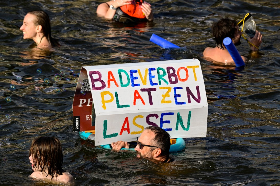 A participant swims with a placard with the lettering 'Break the bathing ban' while taking a dip in the Spree river during a second swimming demonstration for the abolition of the general swimming ban in the inner-city Spree river in central Berlin on August 12, 2025. They demonstrate for the possibility to swim in the inner-city Spree river again; it was banned around 100 years ago. (Photo by John MACDOUGALL / AFP) (Photo by JOHN MACDOUGALL/AFP via Getty Images)
