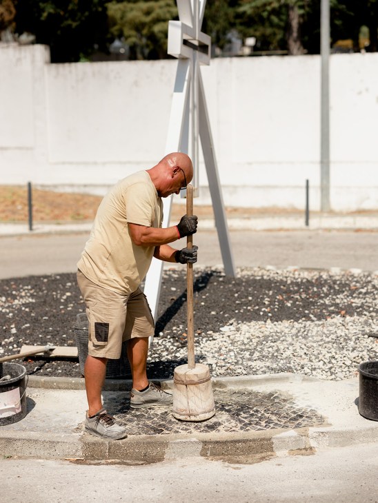 Vítor Graça, a Portuguese calçeteiro, uses a hammer and chisel to lay traditional stone pavement outside a cemetery.