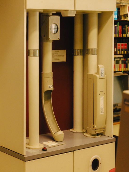 Vintage pneumatic postal tube system with cream-colored cylindrical tubes and brass fittings inside a library display case.
