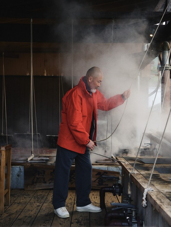 Chef Shinichiro Harakawa wearing a red Jil Sander jacket spraying water in an industrial space.