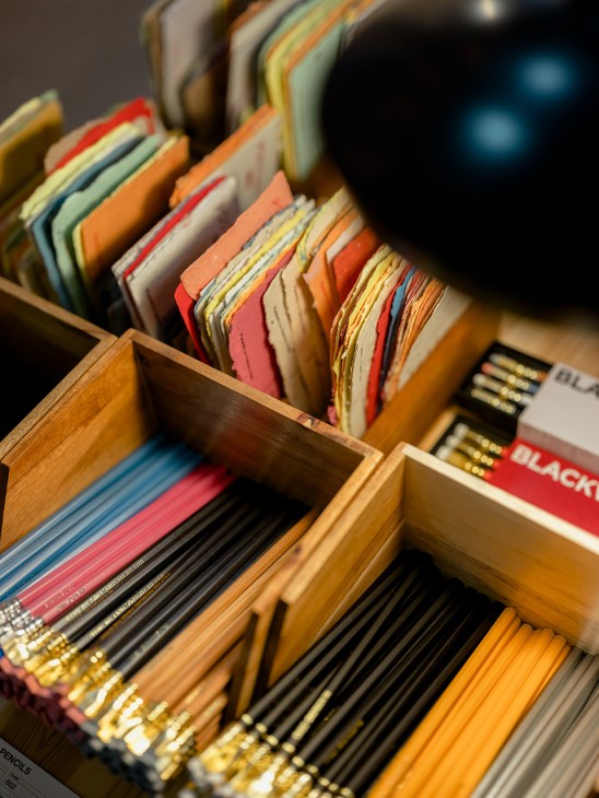 Colorful stationery and pencils arranged in wooden display boxes at O Momento shop.