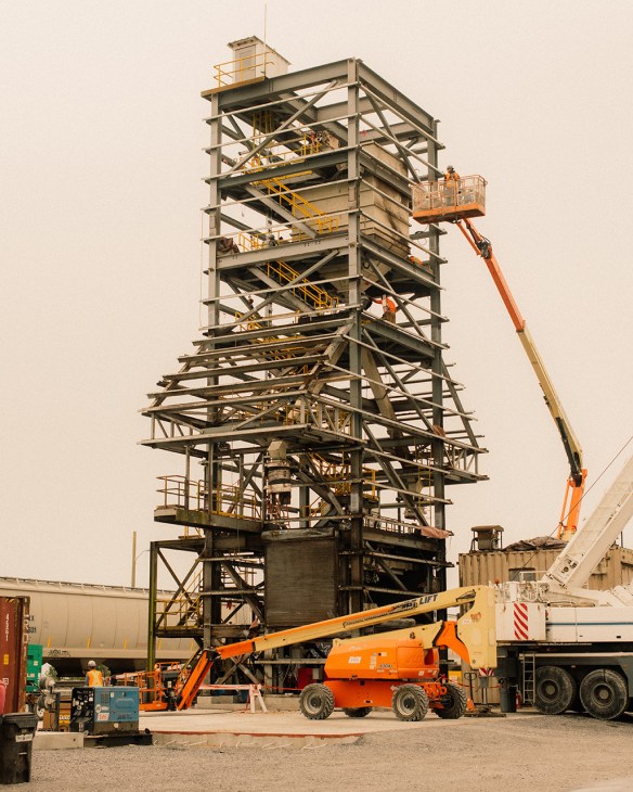 Tall industrial grain silo structure under construction with steel framework and yellow safety railings.