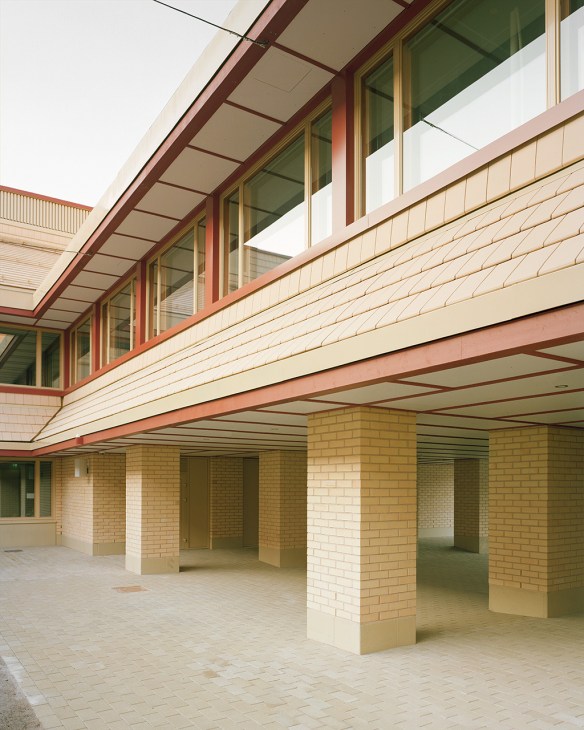 Modern school building with brick columns, red beams, and expansive covered courtyard for students.