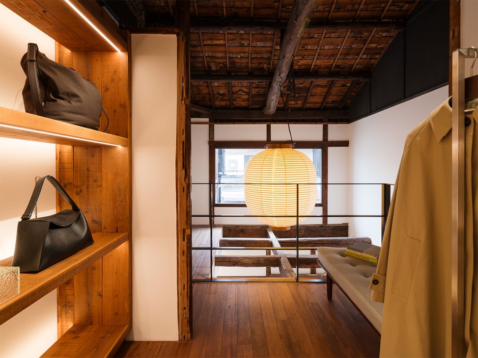 Interior of Studio Nicholson's Kyoto shop with wooden shelves, black bags, yellow coat, and glowing sphere pendant light.