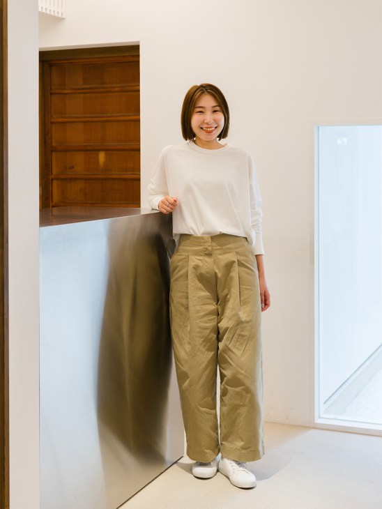 Woman in white long-sleeve top and beige trousers standing in Studio Nicholson's minimalist shop space.