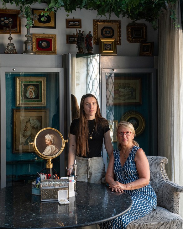 Two women stand in front of display cases filled with religious artwork and artifacts at Savelli Religious shop in Rome.