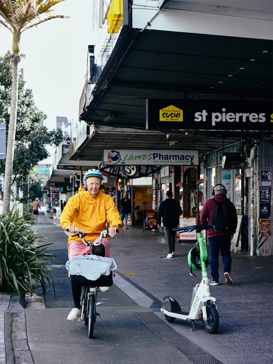 Person in yellow jacket riding a bike with a cargo basket on K' Road in Auckland.