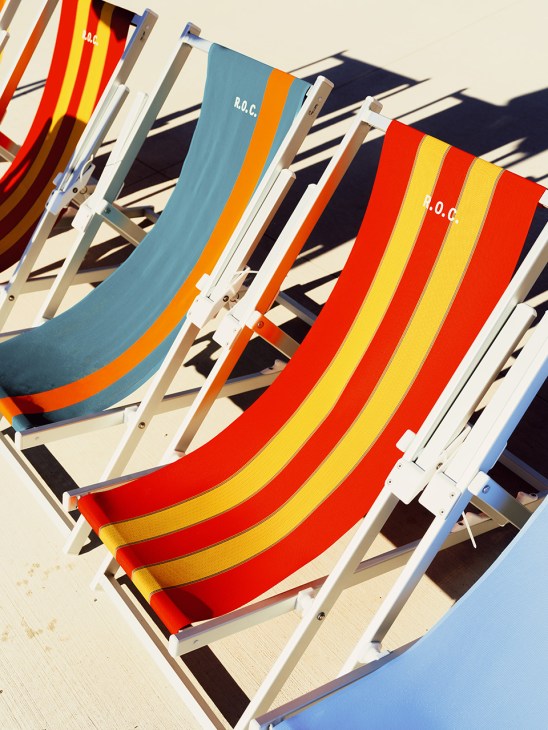Colorful striped beach loungers with white frames arranged in rows on a sunny beach.