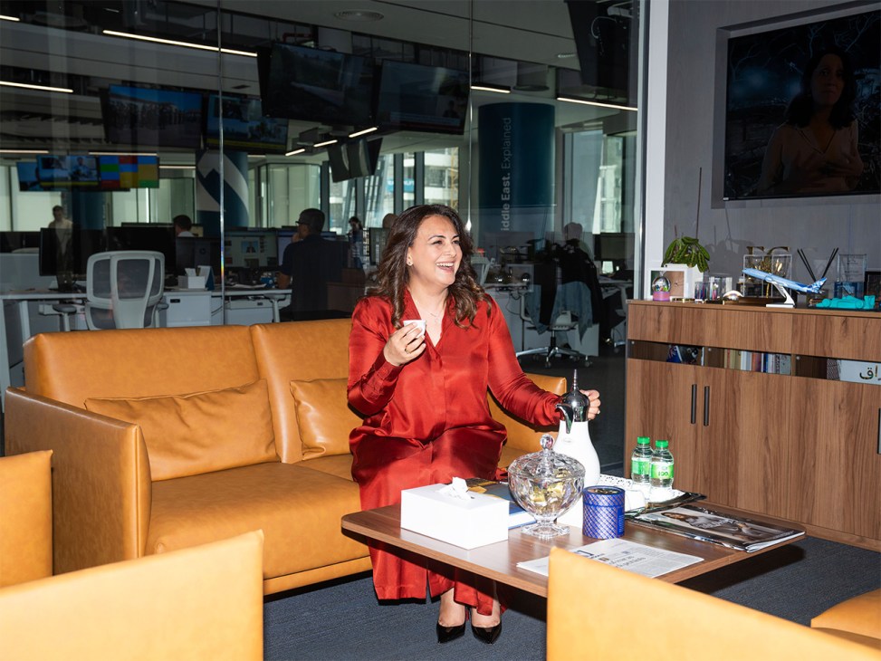Mina Al-Oraibi, editor in chief of The National, sits on an orange leather sofa in her Abu Dhabi office wearing a red outfit.