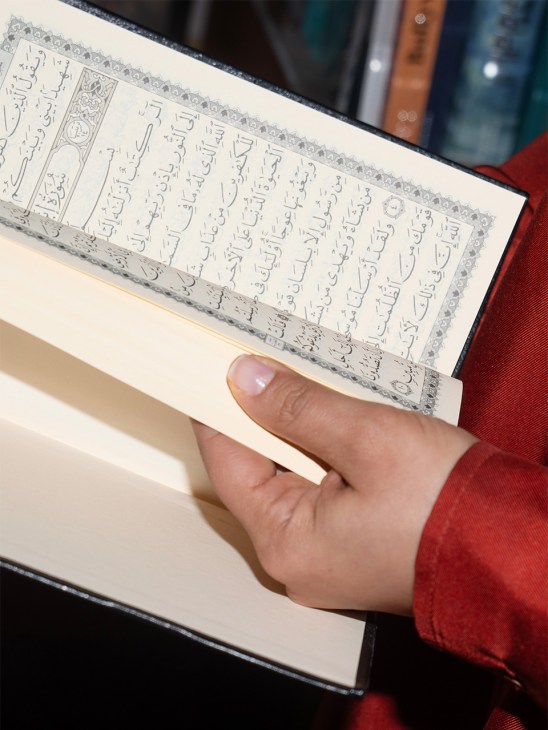 Person in red sleeve holding open a Quran with decorative border and Arabic text.