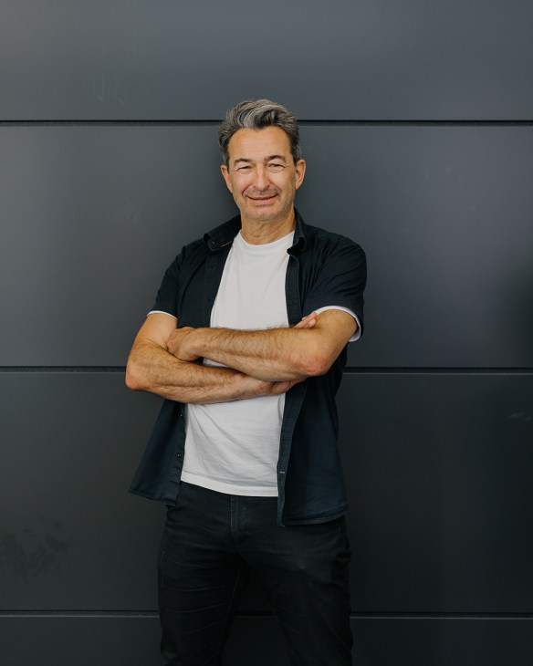 Man with crossed arms wearing white t-shirt and black jacket against gray wall