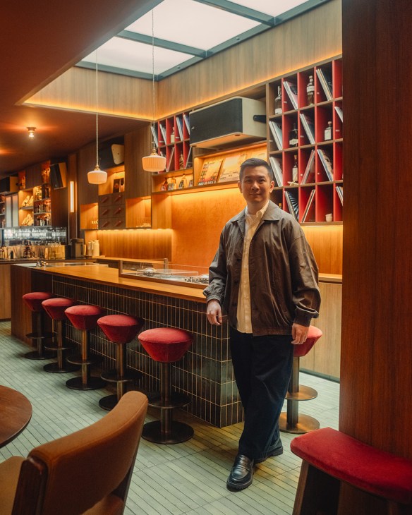 Indra Kantono stands in Pop City cocktail bar, surrounded by warm orange lighting, red bar stools, and bookshelves.