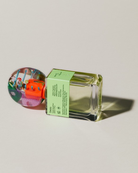 Oddity fragrance bottle with green label next to colorful spherical object on white surface