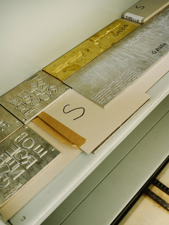 Brass dies with embossed text and patterns for hot-foil stamping arranged on a white surface