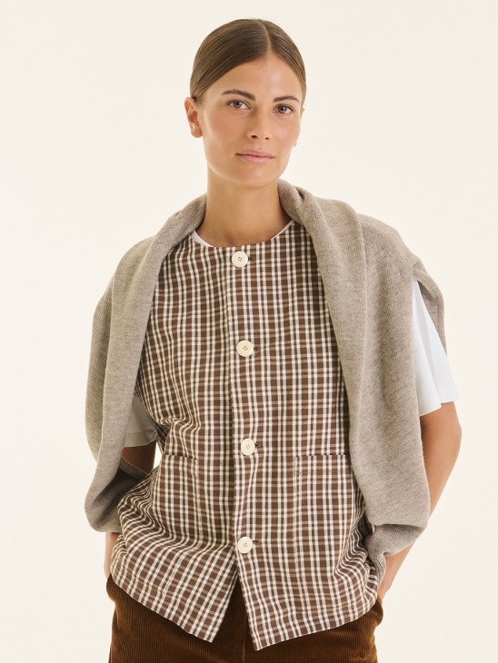 Woman wearing a beige cardigan over a brown and white gingham button-up shirt by Maison Douillet