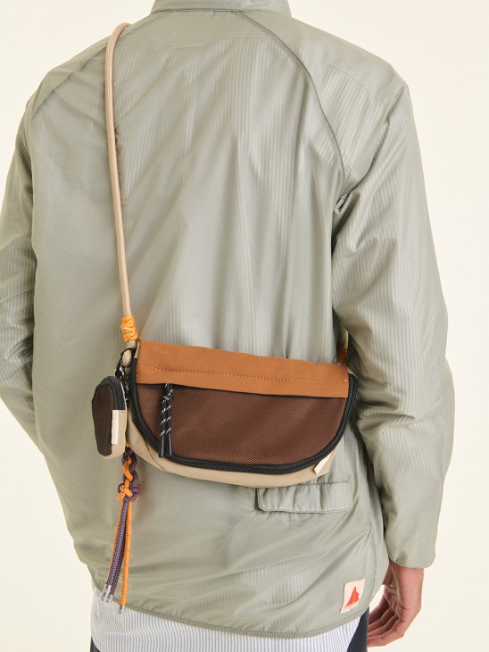 Person wearing beige anorak and tan shoulder bag with mesh pocket and orange strap by Nappa Dori.