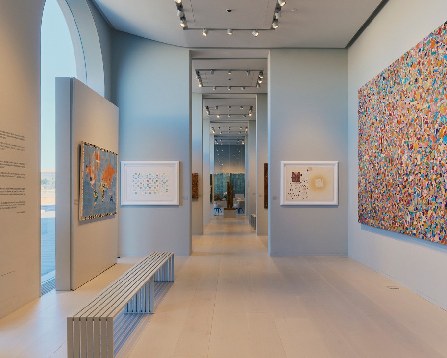 Modern gallery interior with colorful abstract artworks displayed on white walls and track lighting.