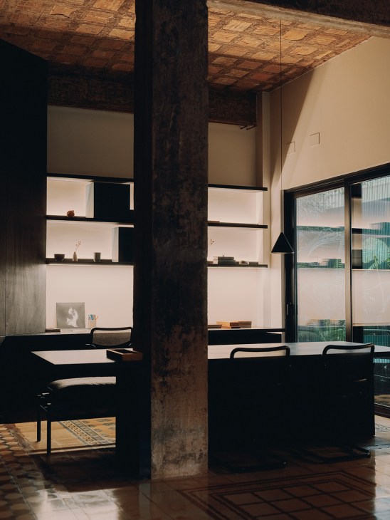 Modern minimalist home office with illuminated shelving, dark structural column, and pendant lighting in Finca Roja.