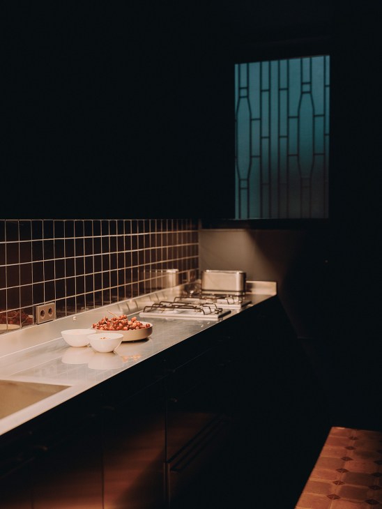 Modern kitchen counter with white bowls containing red peppers, dark tiled backsplash, and gas cooktop in background