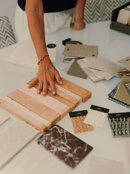 Hand touching wood material samples on a table with fabric swatches and design samples nearby