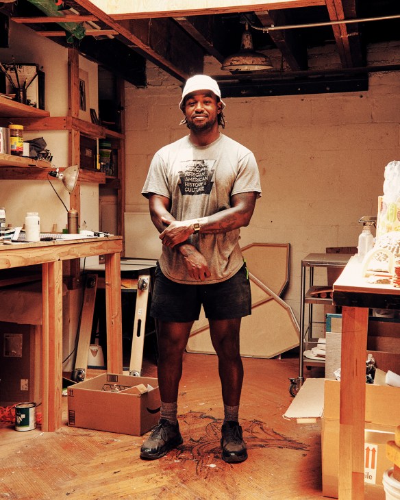 Woodworker Mike Haynes standing in his workshop wearing a white cap and gray t-shirt.