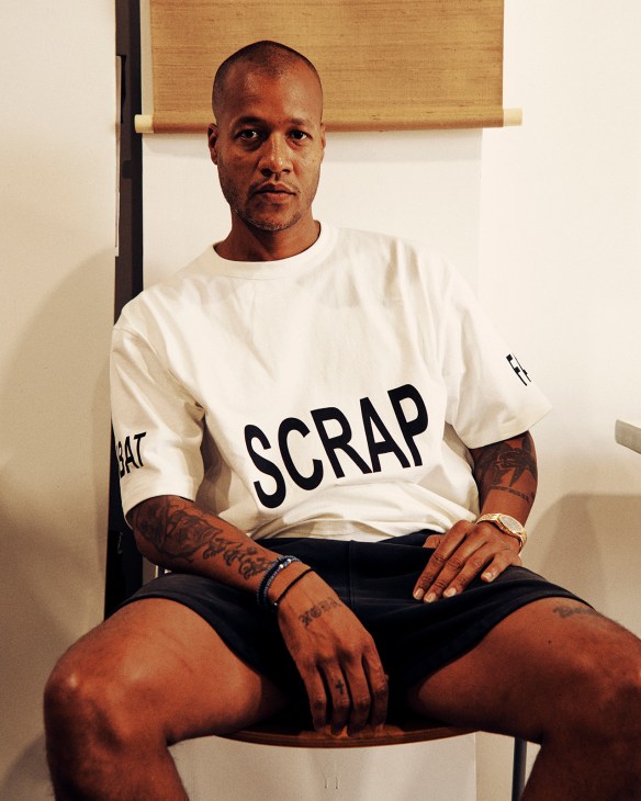 Streetwear designer Heron Preston wearing a cream SCRAP t-shirt and black shorts in his Red Hook studio.